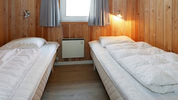 Et værelse med to senge, trævægge, et vindue med gardiner og en fastmonteret varmeovn.