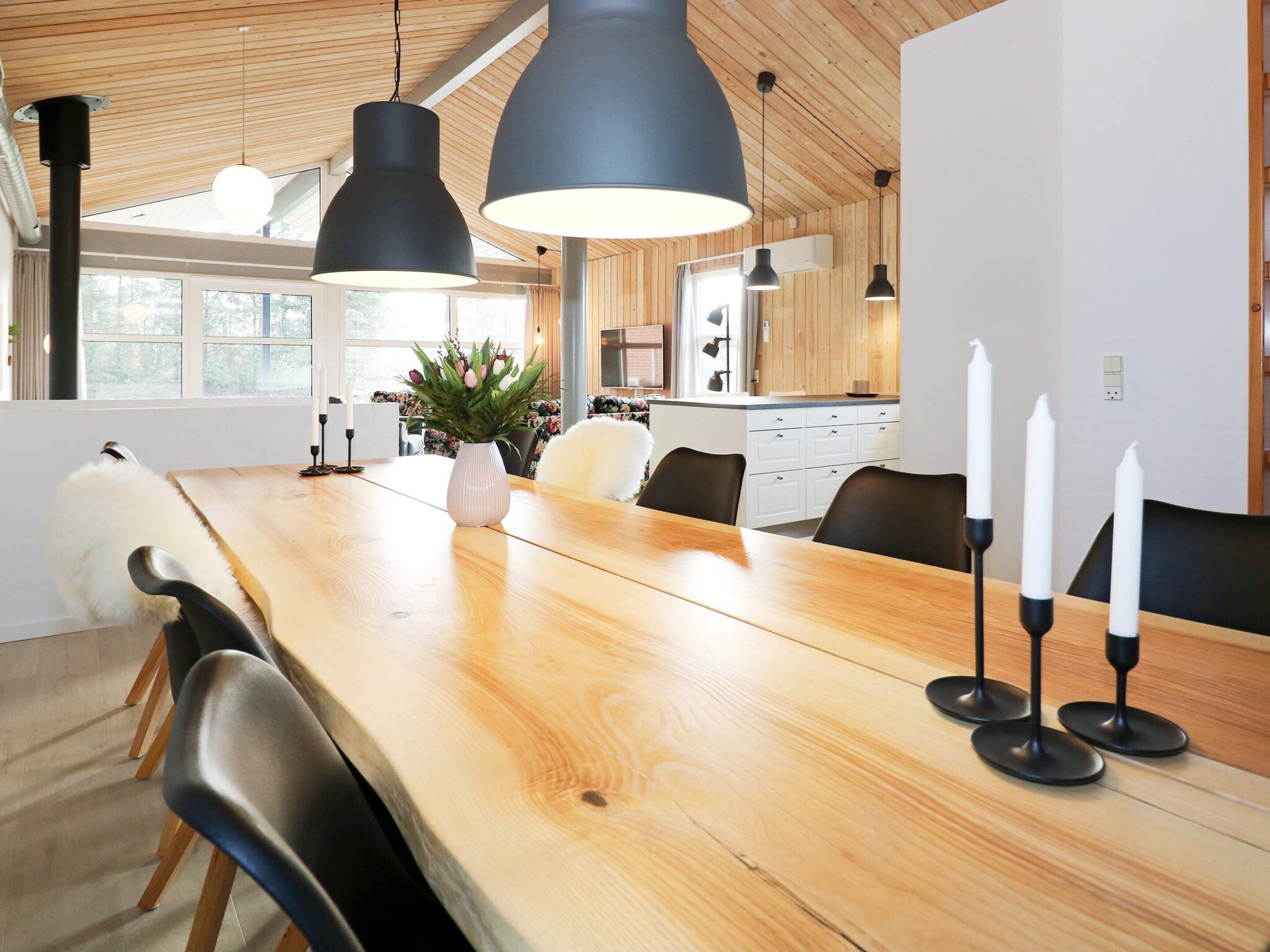 Et moderne spiseområde med et træbord, sorte stole og hængende lamper.