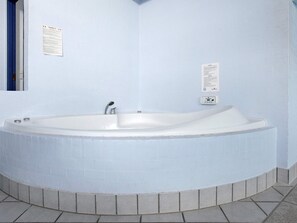 A large, empty bathtub in a corner of a room with light blue walls and a tiled floor. - 5 Star Holiday Home in Hadsund (Hadsund)