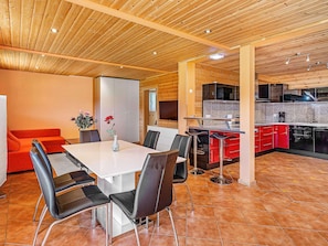 A modern kitchen with wooden ceiling, red cabinets, and a dining area with a white table and black chairs.