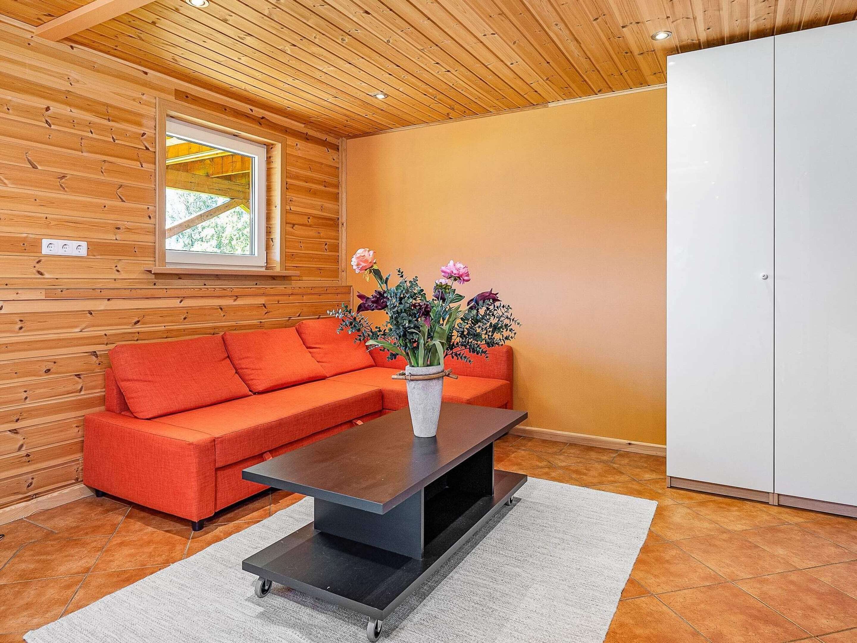 Un interior moderno con techo de madera, un sofá rojo, un armario blanco y un florero sobre una mesa.