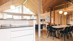 A modern kitchen with a large island, dining area with chairs, wooden ceiling, and pendant lights.