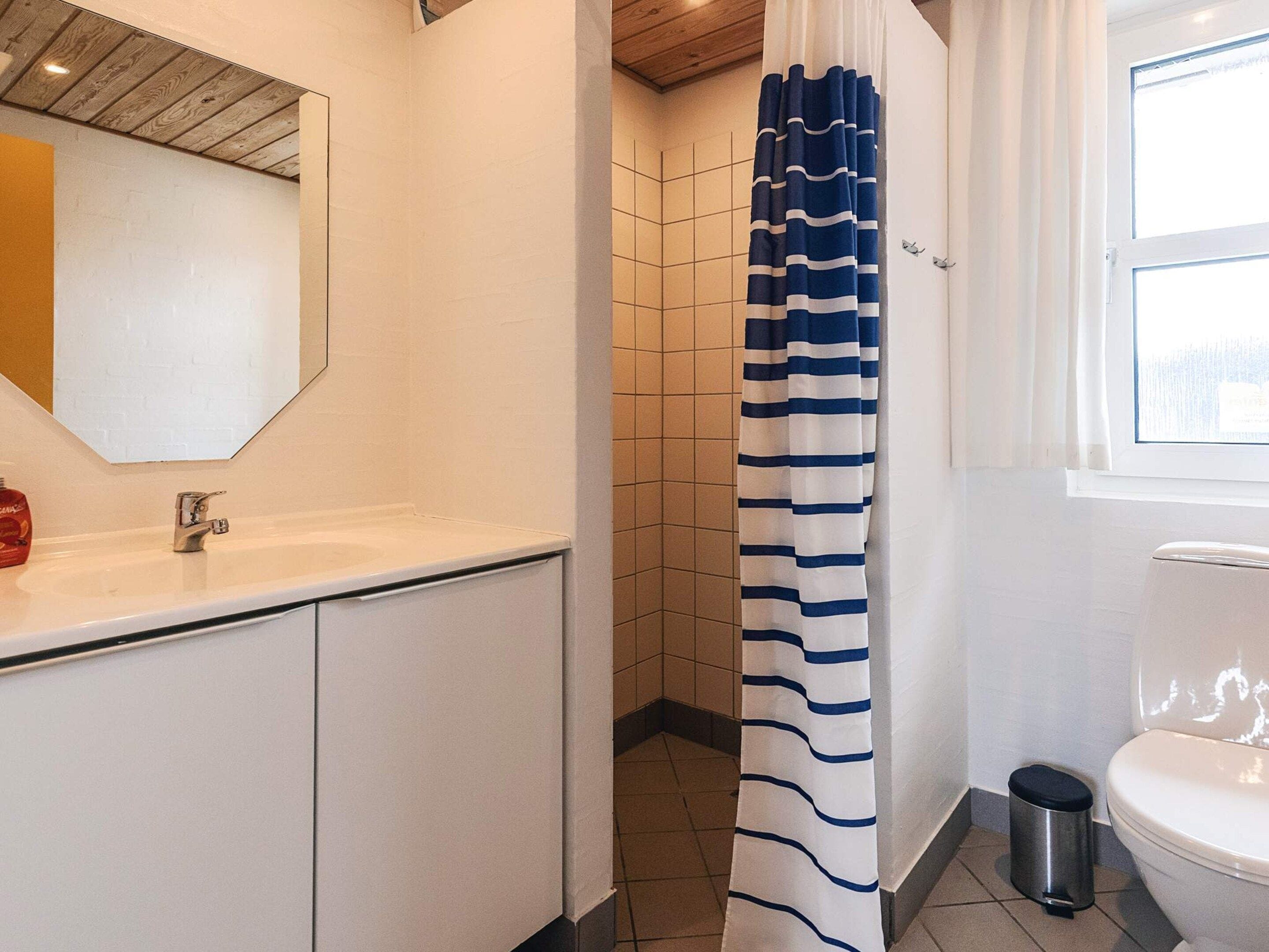 Een badkamer met douchegordijn, toilet, wastafel en spiegel.