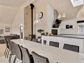 A modern kitchen with a dining area, featuring a long table, chairs, pendant lights, and a clock on the wall. - 5 Star Holiday Home in Vejby (Vejby)