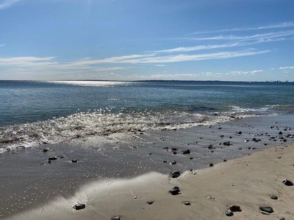 A beach with a clear sky, calm sea, and scattered rocks.