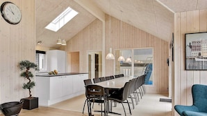 A spacious dining area with a long table and chairs, a kitchen with white cabinets, and a large window. - 5 Star Holiday Home in Vejby (Vejby)