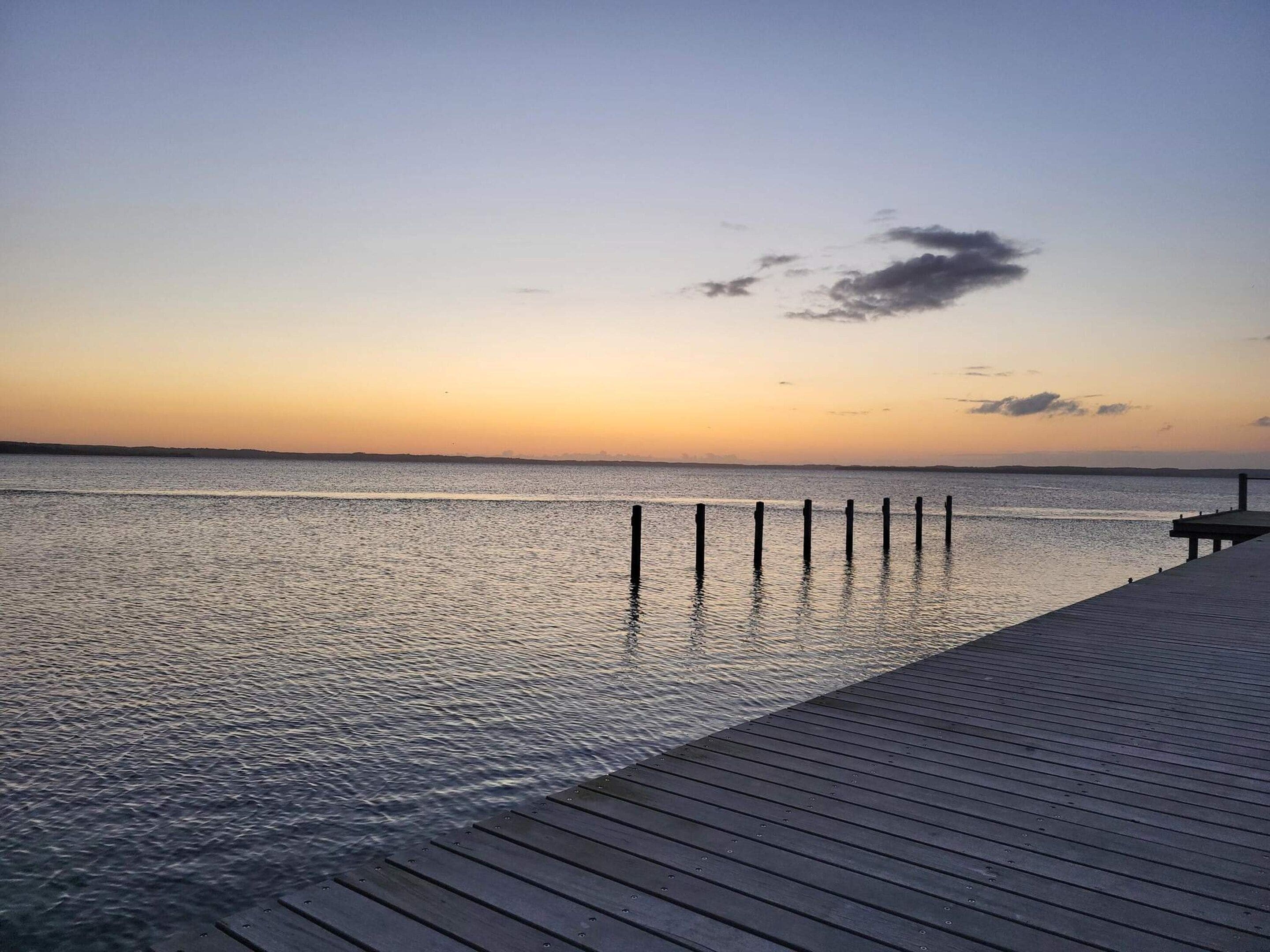 A wooden pier extending into calm water with a clear sky above.