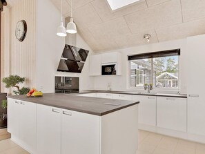 A modern kitchen with a central island, white cabinetry, a microwave, and a large window. - 5 Star Holiday Home in Vejby (Vejby)