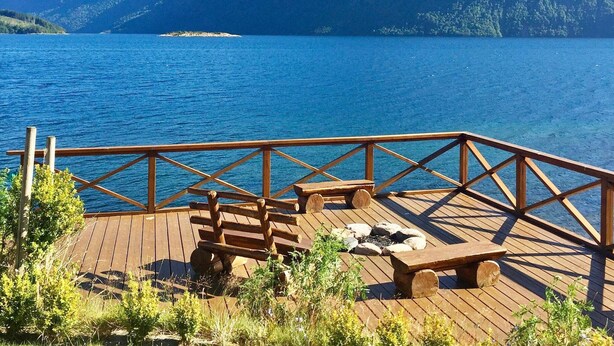A wooden deck with benches overlooking a lake and mountains.