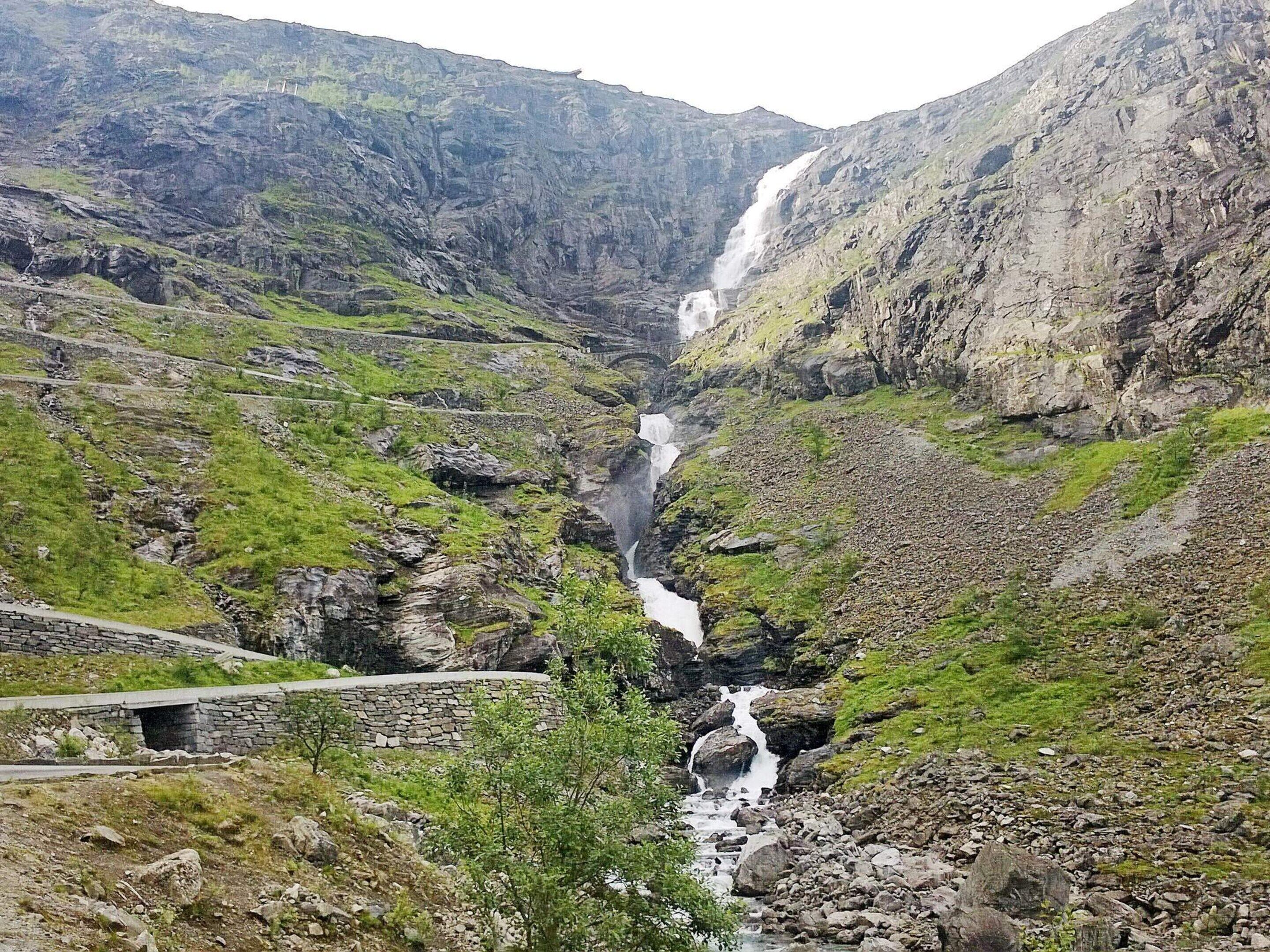 Ett bergigt landskap med ett vattenfall, stenigt område och en stenbro.