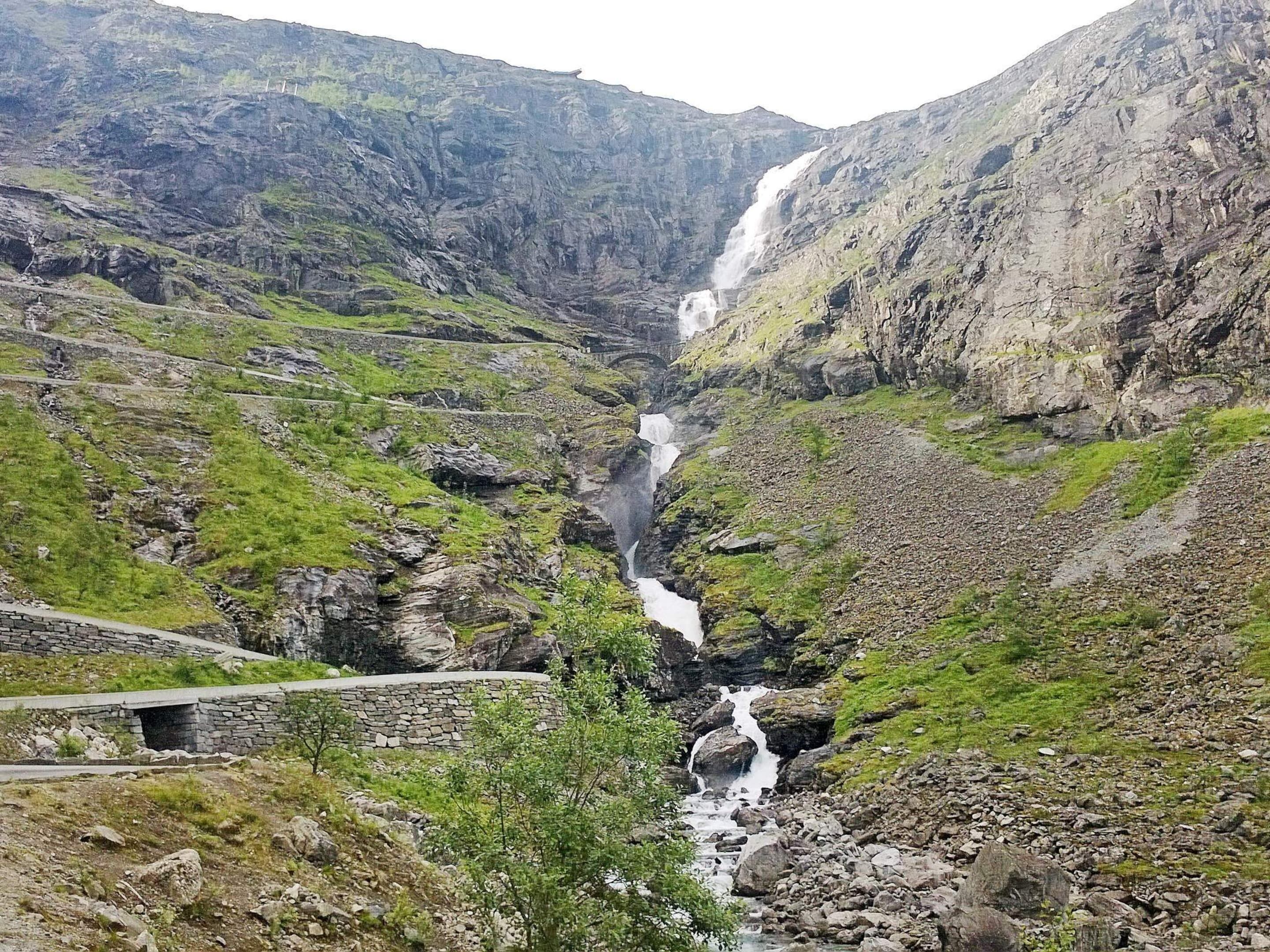 A mountainous landscape with a waterfall, rocky terrain, and a stone bridge.