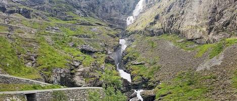 A mountainous landscape with a waterfall, rocky terrain, and a stone bridge.