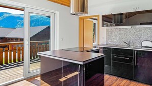A modern kitchen with a large window, a view of mountains, and a wooden ceiling.