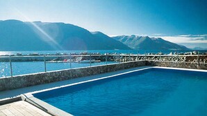 A swimming pool with a wooden deck, surrounded by a stone wall, with mountains in the background.