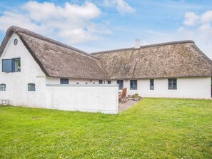 A traditional thatched-roof house with a white exterior, a small garden, and a clear sky.