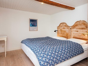 A bedroom with a wooden headboard, a bed with a floral bedspread, a small bedside table, and a framed picture on the wall.