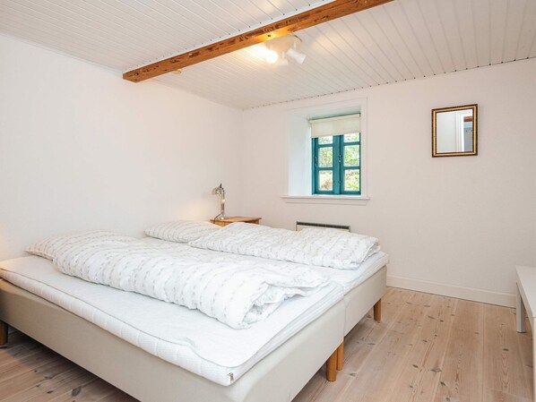 A bedroom with a bed, a bedside table, a lamp, a window, and a mirror.