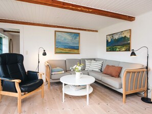 A living room with a sofa, a black leather chair, a white coffee table, and two paintings on the wall.