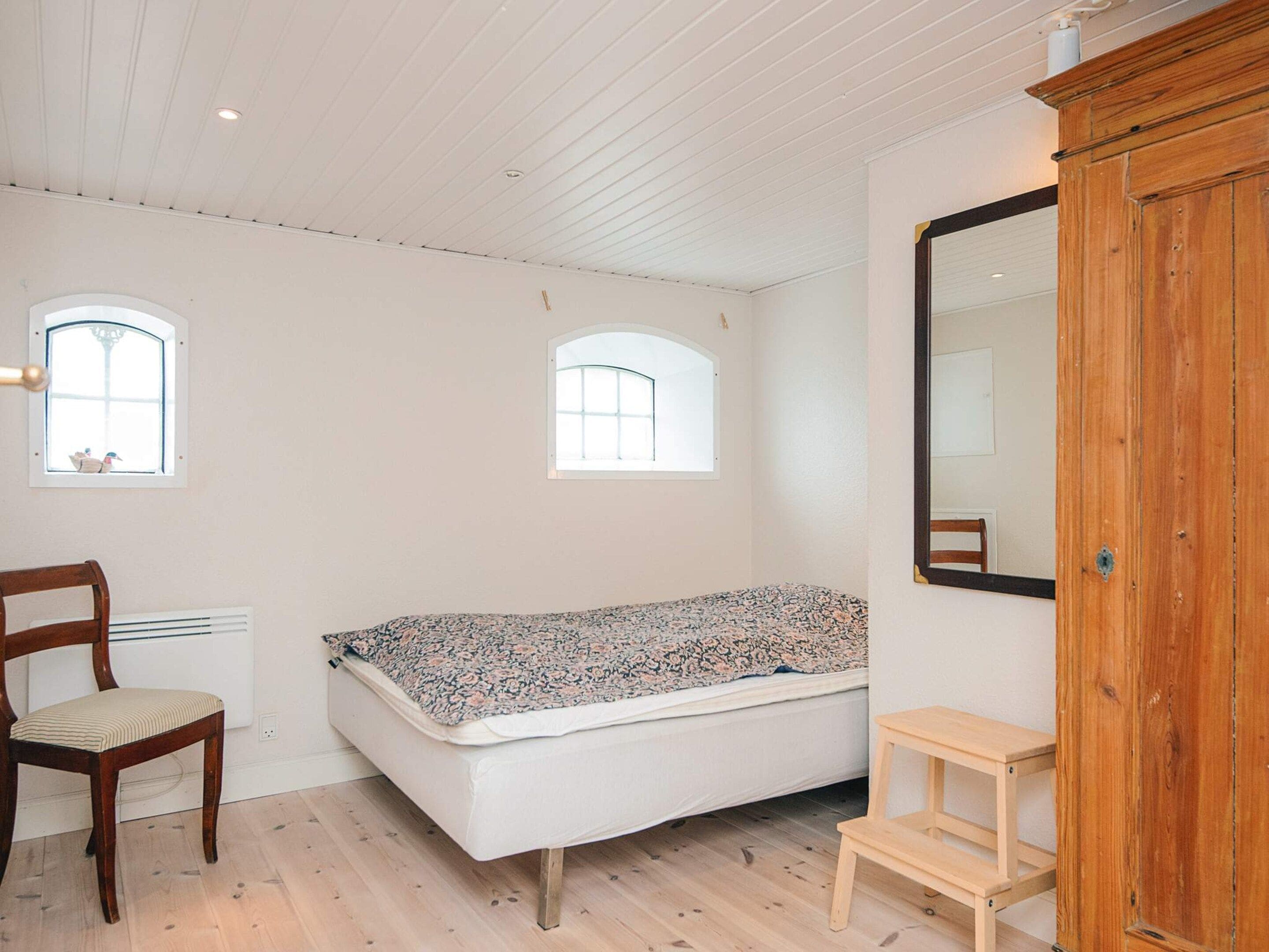 A room with a bed, a chair, a small table, and a large mirror.
