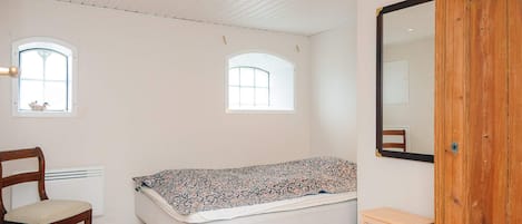 A room with a bed, a chair, a small table, and a large mirror.