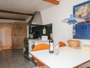 A kitchen with a stove, oven, and a dining table with a bottle of wine and a glass.