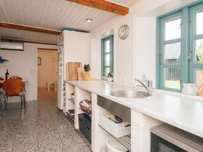 A kitchen with a sink, wooden cutting board, and a clock on the wall.