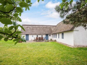 A thatched-roof building with a white exterior, a grassy courtyard, and a dining area with chairs and tables.
