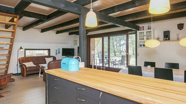 A spacious living area with a wooden ceiling, a large window, a brown leather sofa, a TV, and a dining area with a wooden table and chairs. - Tranquil Holiday Home in Vestervig near Sea (Vestervig)