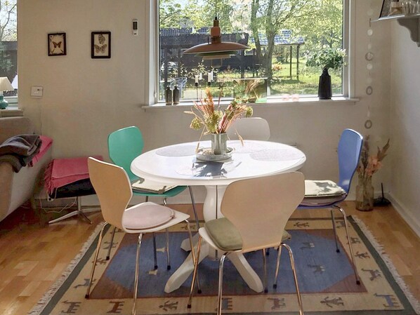 A dining area with a round table, four chairs, a vase with flowers, and a view of the outdoors through a window.