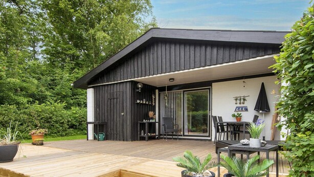 A modern house with a wooden deck, a sliding glass door leading to a patio, and potted plants. - 5 Person Holiday Home in Vinderup (Vinderup)