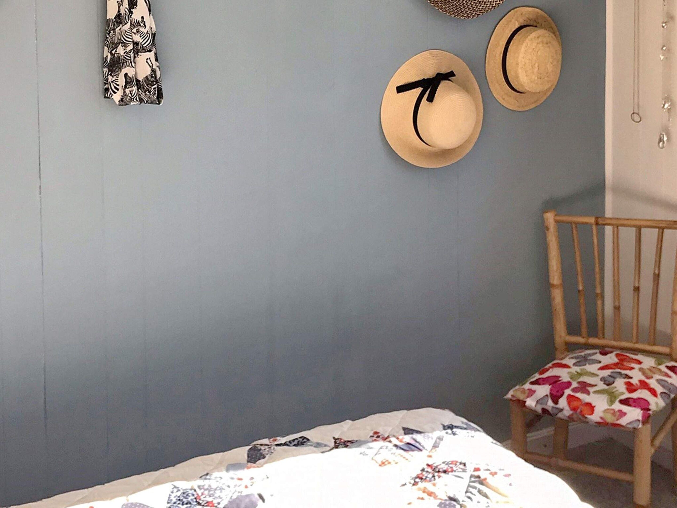 A bedroom with a bed, a chair, and two hats on the wall.