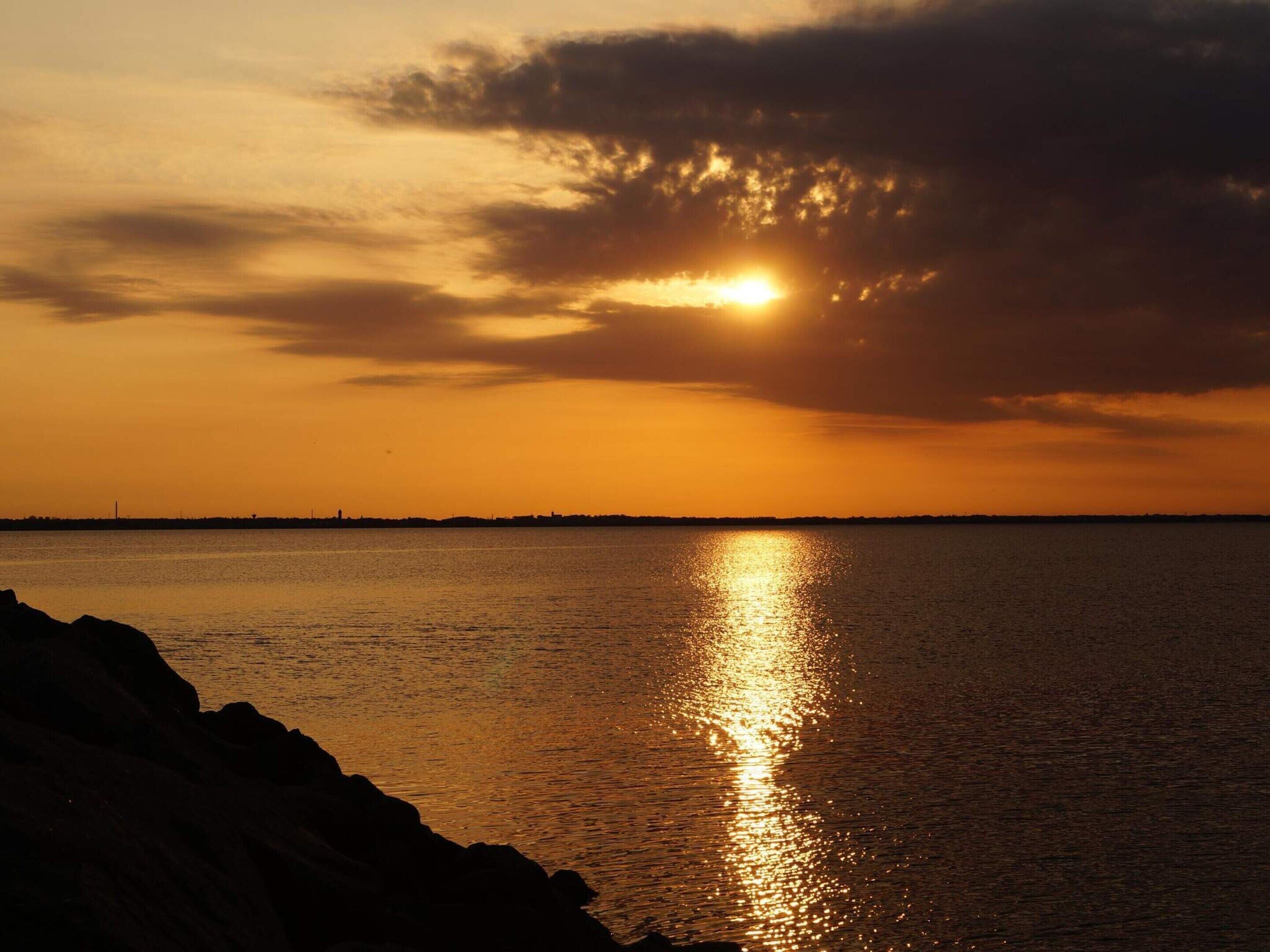 A sunset over a calm body of water with a silhouette of a rocky shoreline.