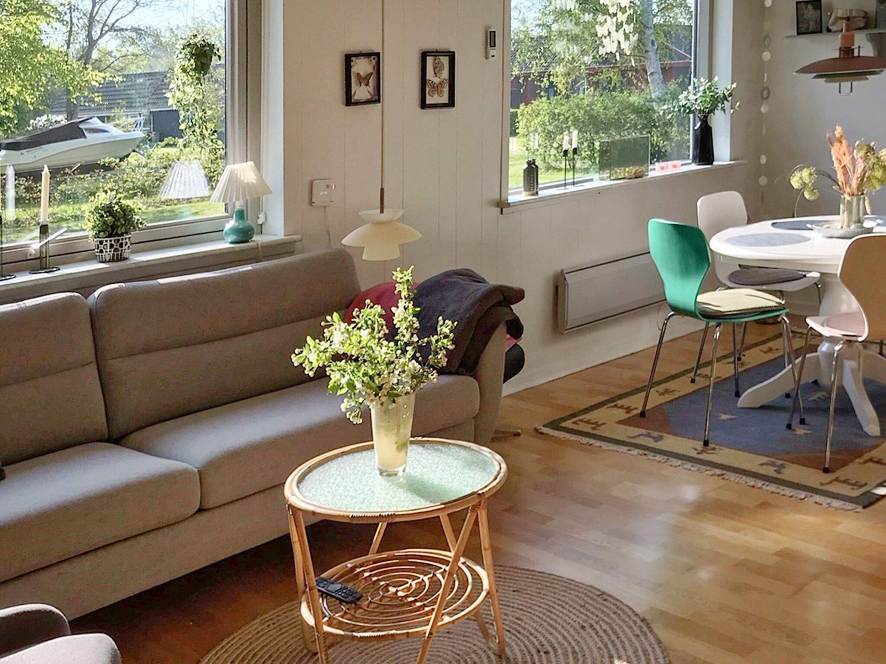 A living room with a sofa, a round table with chairs, a small round table with a vase of flowers, and a window with a view of the outdoors.