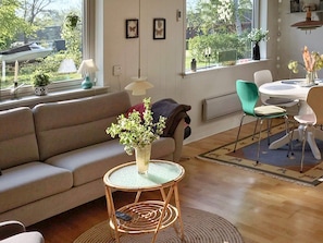A living room with a sofa, a round table with chairs, a small round table with a vase of flowers, and a window with a view of the outdoors.