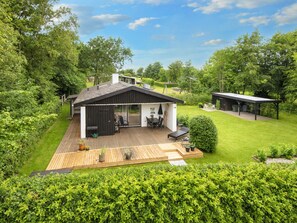 A modern house with a deck, a covered patio, and a well-maintained lawn.
