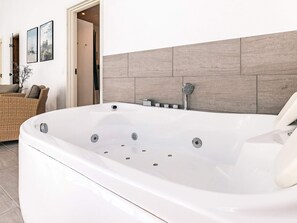 A modern bathroom with a large white bathtub, a showerhead, and a tiled wall. - 5 Star Holiday Home in Thisted (Thisted)