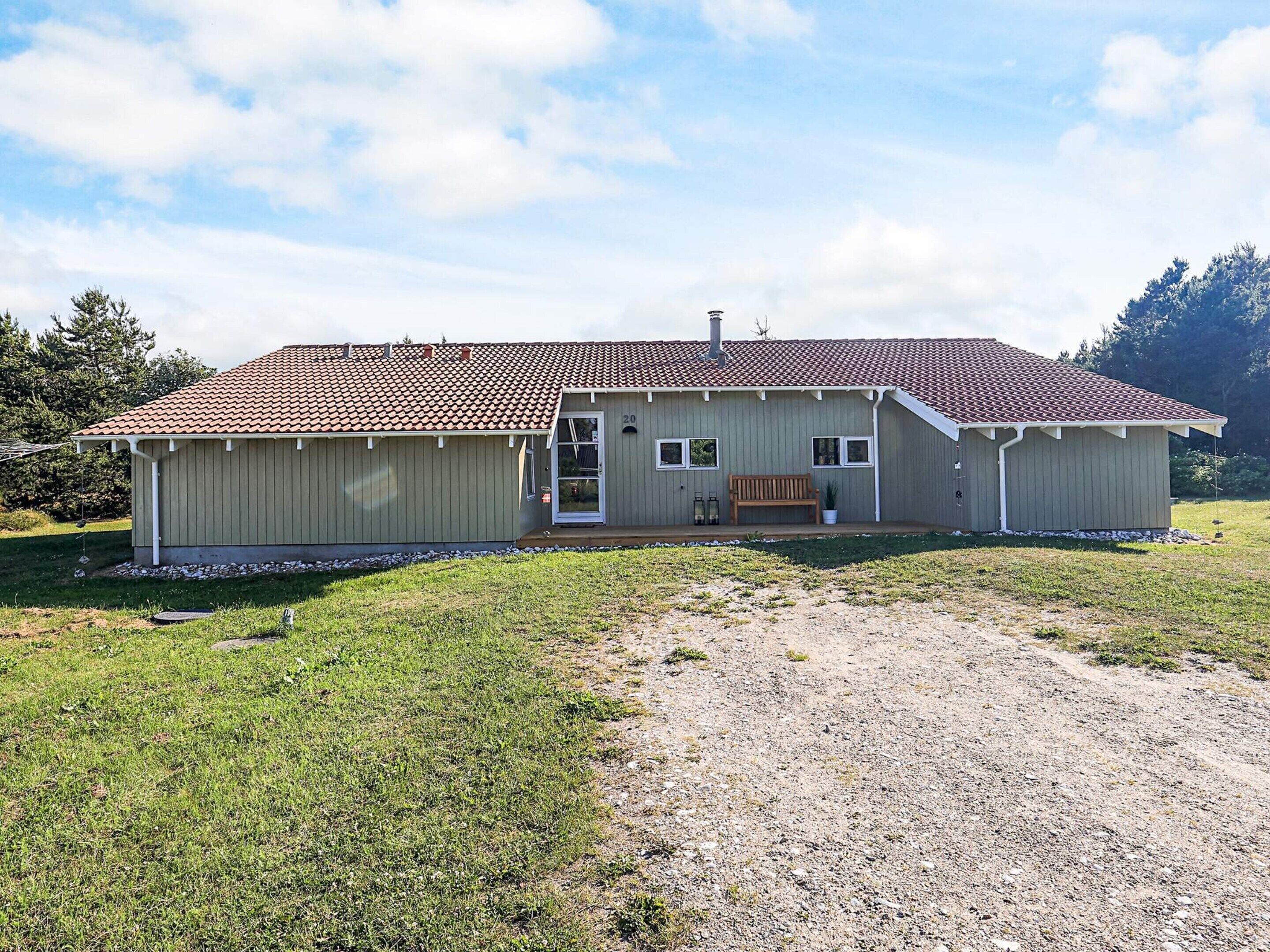A single-story house with a tiled roof, a front porch with a bench, and a small garden area.