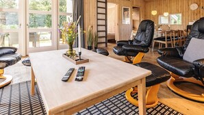 A modern living room with a wooden interior, a dining area with a table and chairs, and a large window offering a view of greenery. - 5 Star Holiday Home in Thisted (Thisted)