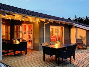 A wooden deck with a dining table and chairs, a covered patio area with string lights, and a view of the interior through glass doors. - 5 Star Holiday Home in Thisted (Thisted)