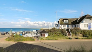 A coastal hotel with a thatched roof, a small adjacent structure, and a view of the sea. - 5 Star Holiday Home in Thisted (Thisted)