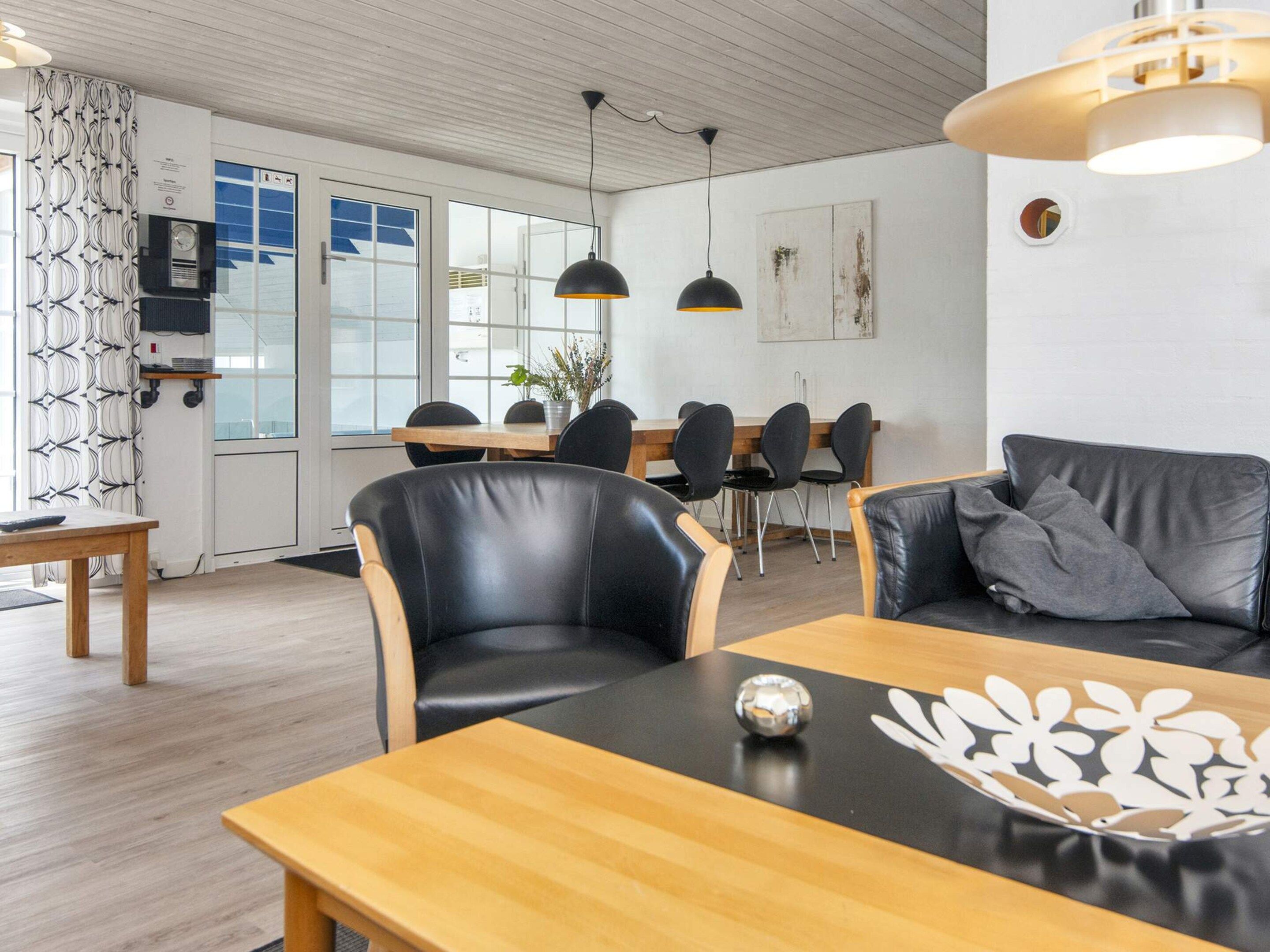 Una sala de estar moderna con una mesa de centro de madera, sillas de cuero negro, un sofá negro con un cojín gris e iluminación colgante.