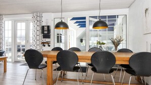 Un comedor moderno con una mesa de madera y sillas negras, ventanas amplias y un techo con vigas a la vista.