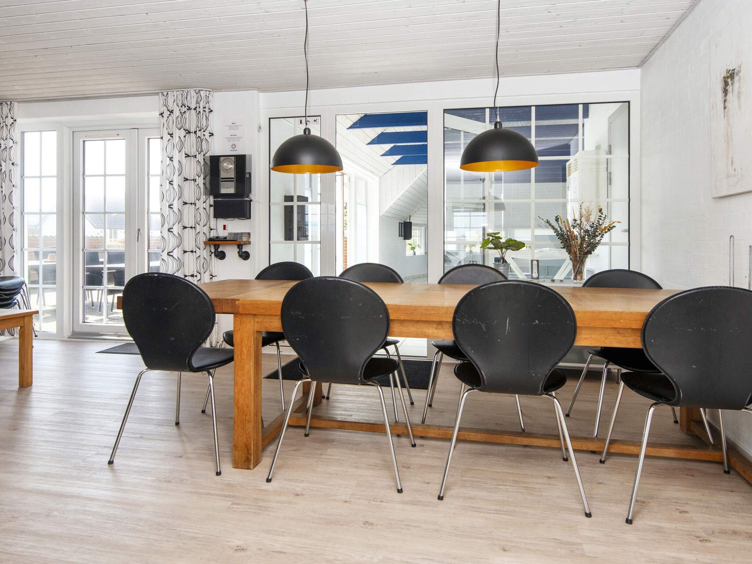 Spiseområde med et træbord og sorte stole, store vinduer og et moderne loftsdesign.