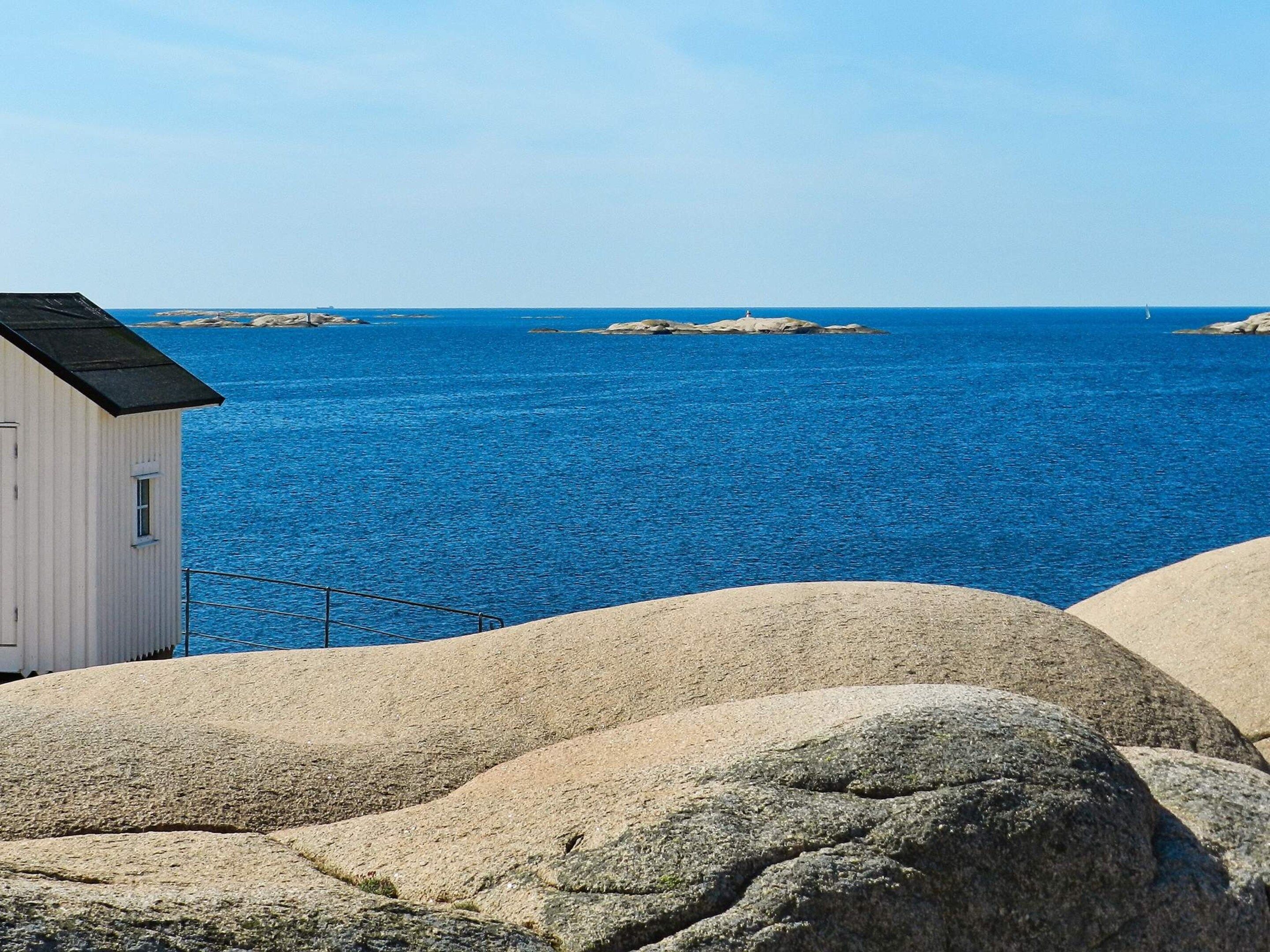 Un paisaje costero con un edificio blanco, rocas grandes y un mar azul transparente.
