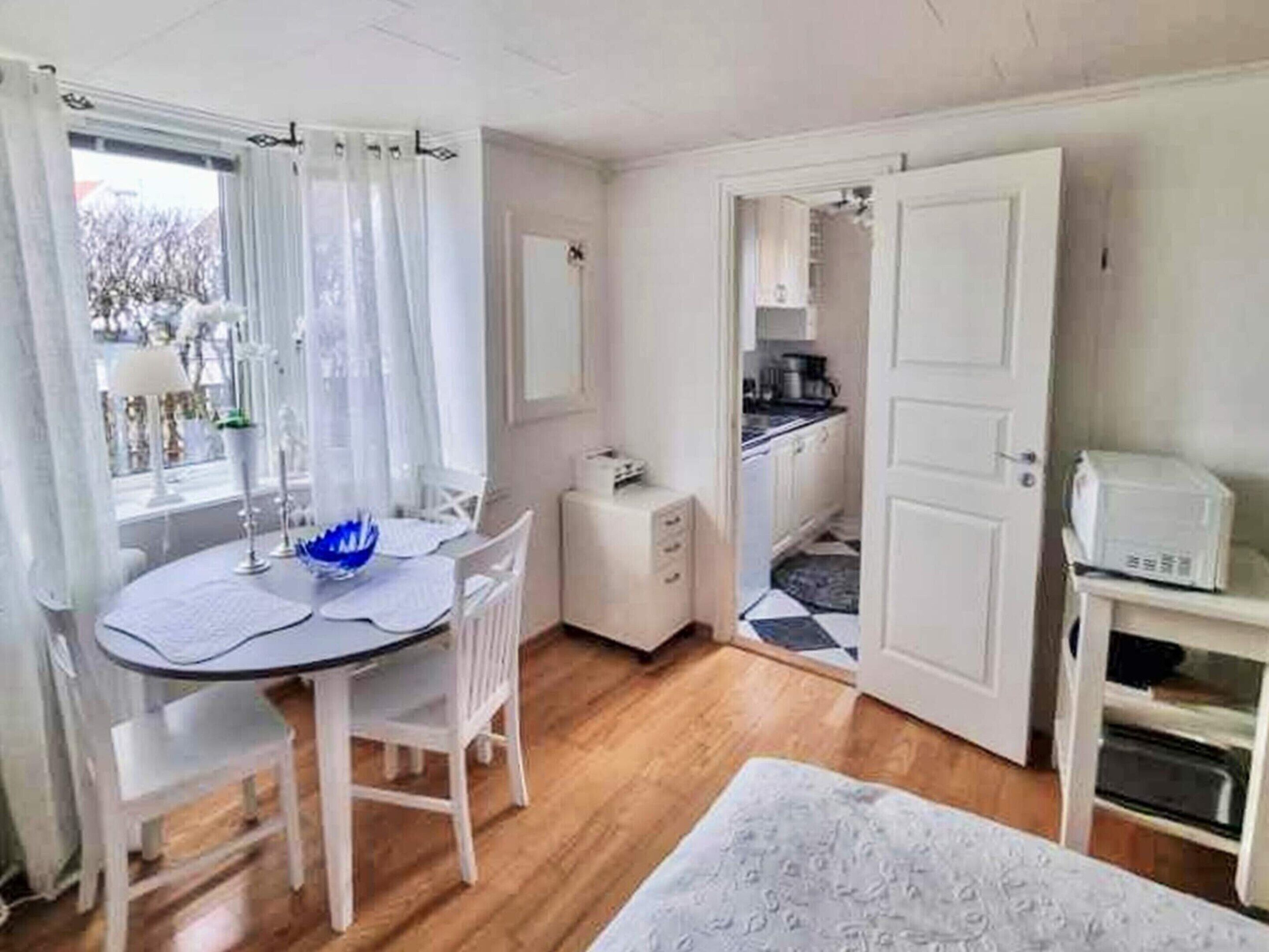 A room with a dining table, chairs, a small kitchenette, and a bed.