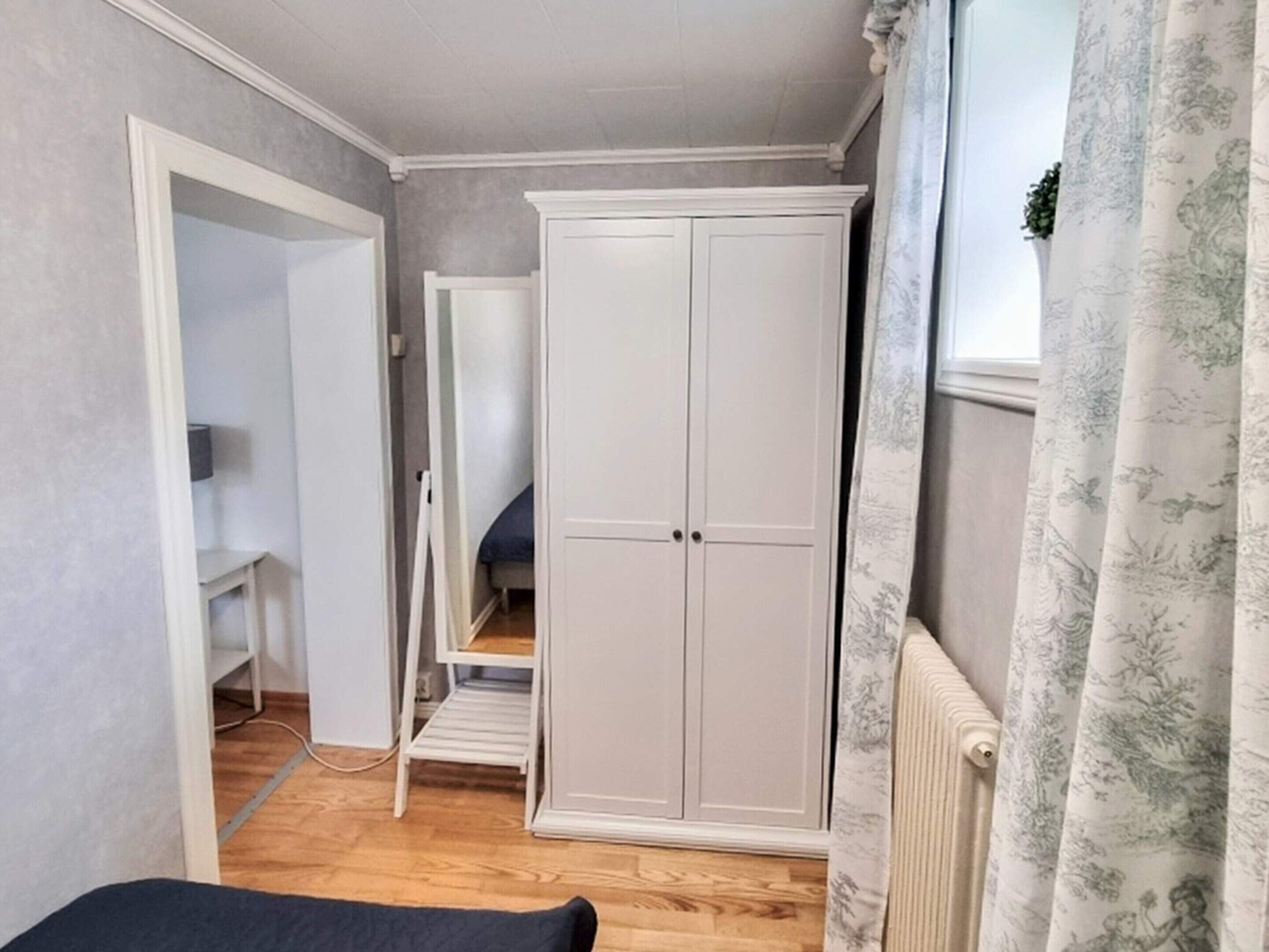 Une chambre avec une armoire, un lit, un radiateur et une fenêtre avec des rideaux.