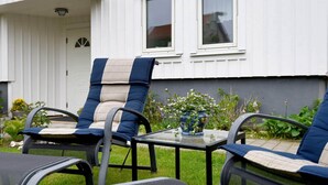 An outdoor seating area with two lounge chairs and a small table, in front of a white building with two windows and a door. - 3 Person Holiday Home in Lysekil (Lysekil)