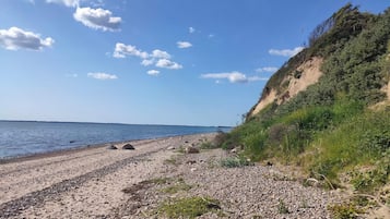 Une plage de galets, un ciel dégagé et une terre lointaine à l’horizon.