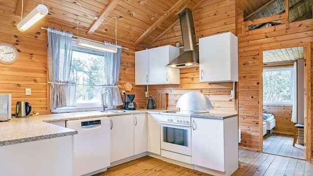 Une cuisine de taille réduite avec des murs en bois, des placards blancs, une cuisinière et une fenêtre avec des rideaux.
