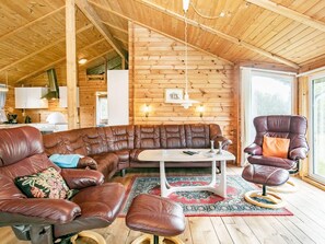 Een gezellig interieur van een blokhut met een hoekbank, een ronde tafel en leren fauteuils.